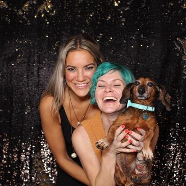 Two girls laughing and smiling, one holding up a dog