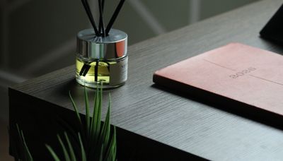 A table with a reed diffuser, a pink notebook, and a plant.