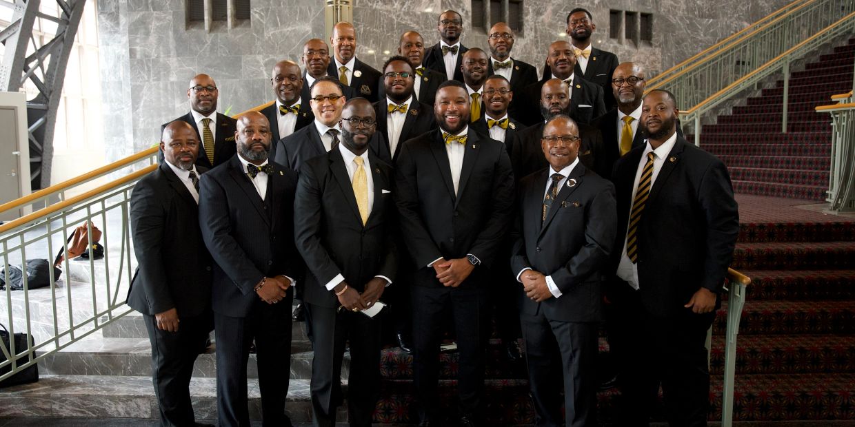 Group of men dressed in suits posing on stairs.