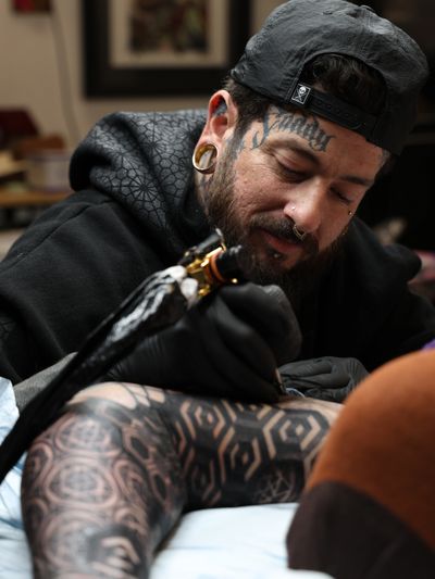 Tattoo Artist using a tattoo machine to tattoo geometry on an arm
