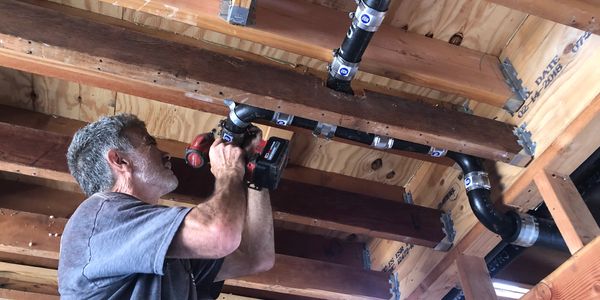 A man using an electric drill to install pipes.