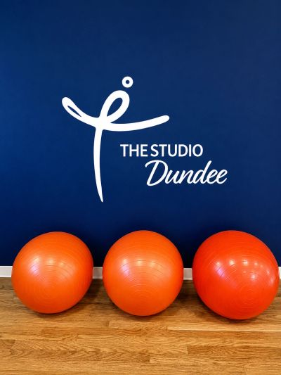 Three orange exercise balls in front of a blue wall with "The Studio Dundee" logo.