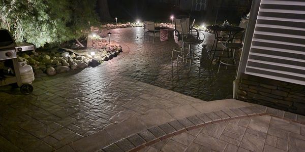 Backyard patio at night with stone flooring and outdoor furniture.