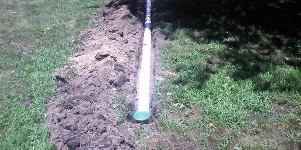 A long pipe being installed in a dug trench in a backyard.
