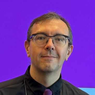 Man wearing glasses and a tie with purple background.