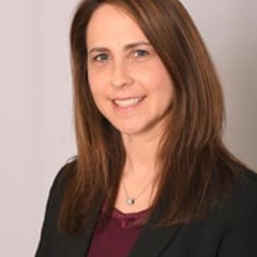 Professional woman smiling with straight brown hair, wearing a black blazer.