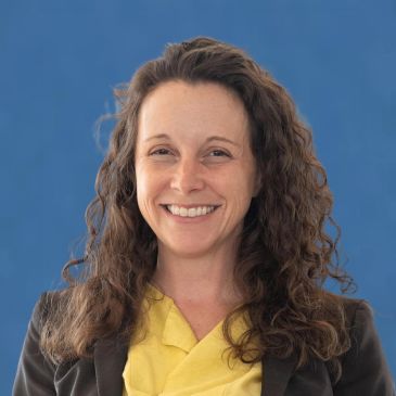 Smiling woman with curly hair against blue background.