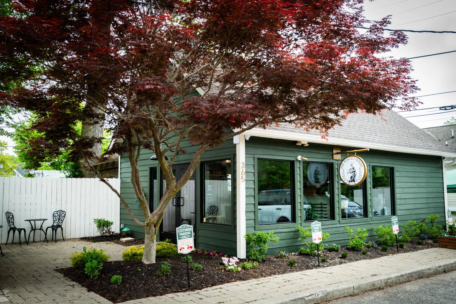 A quaint green bakery with outdoor seating and red-leafed trees.