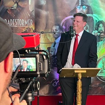 A man in a suit speaks at a podium while being recorded.