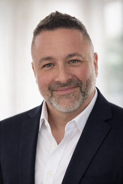 Smiling man in a dark blazer and white shirt with a trimmed beard.