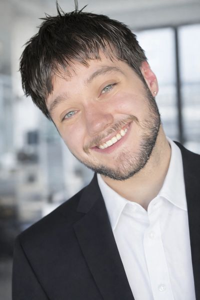 Smiling young man in a suit with a light beard and blue eyes.