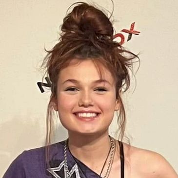 Smiling young woman with hair in a messy bun and casual outfit.