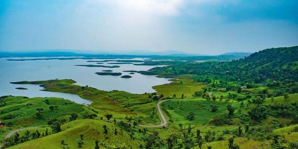 Scenic view of a winding road through green hills beside a large lake under a clear blue sky.