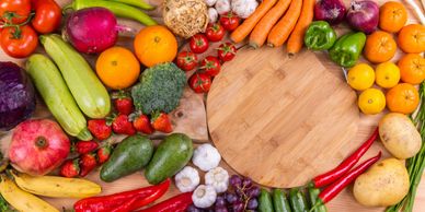 Colorful assortment of fresh fruits and vegetables arranged around a wooden cutting board.