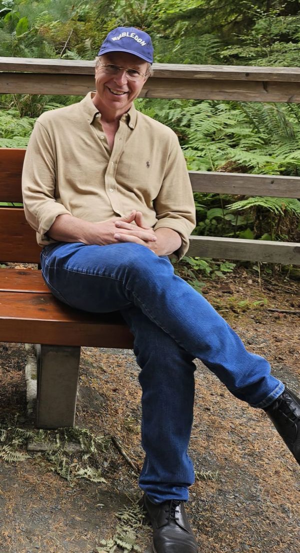 Man sitting on a bench smiling in a green outdoor setting.