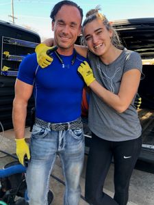 Two friends smiling, wearing work gloves.