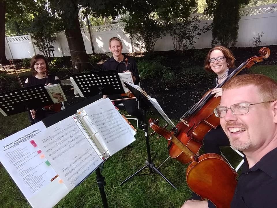 Group playing string instruments outdoors with sheet music.