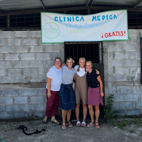 Four women standing in front of a clinic sign that says free medical clinic in Spanish.