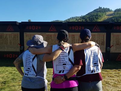 Three friends with race bibs hugging outdoors.