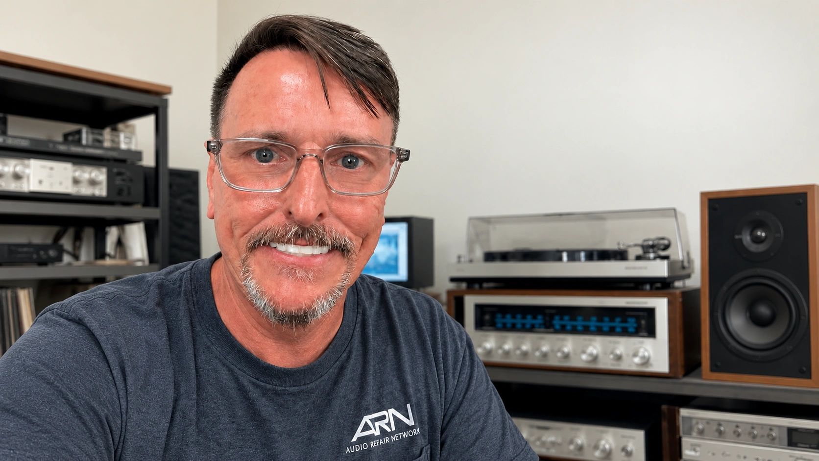 Man smiling with vintage audio equipment in background.