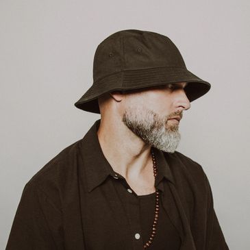 Man wearing a black bucket hat and dark clothing, looking sideways.