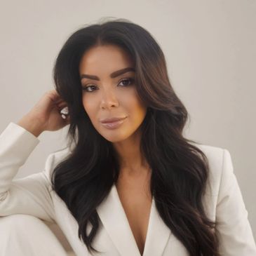 Confident woman with long dark hair in a white blazer poses gracefully.