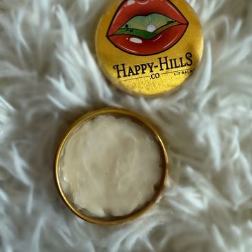 Happy Hills lip balm tin with a colorful lips logo on a soft white surface.