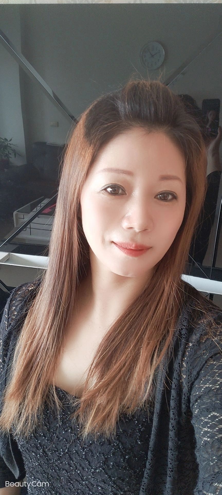 A woman with long hair wearing a black lace top smiles gently.