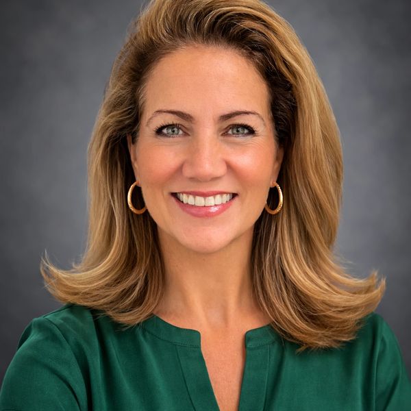 Smiling woman with blonde hair in a green blouse and gold hoop earrings.