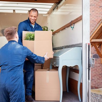 Removal Company Workers Unloading Furniture And Boxes From Truck Into New Home On Moving Day
