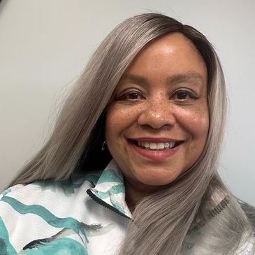 Smiling woman with long gray hair and a patterned jacket.