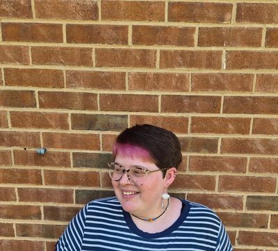 Person with pink hair highlights smiling against a brick wall.