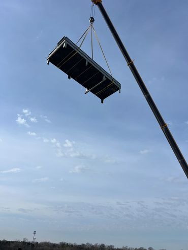 A crane lifts a large black container against a blue sky.