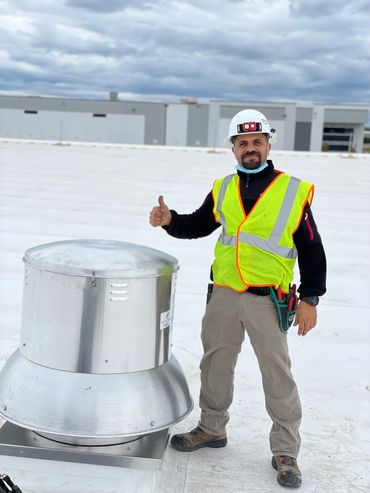 Construction worker giving a thumbs-up on a rooftop with ventilation equipment.