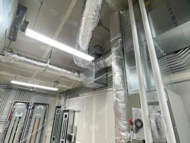 Ceiling with insulated HVAC ducts and lighting fixtures in an industrial room.