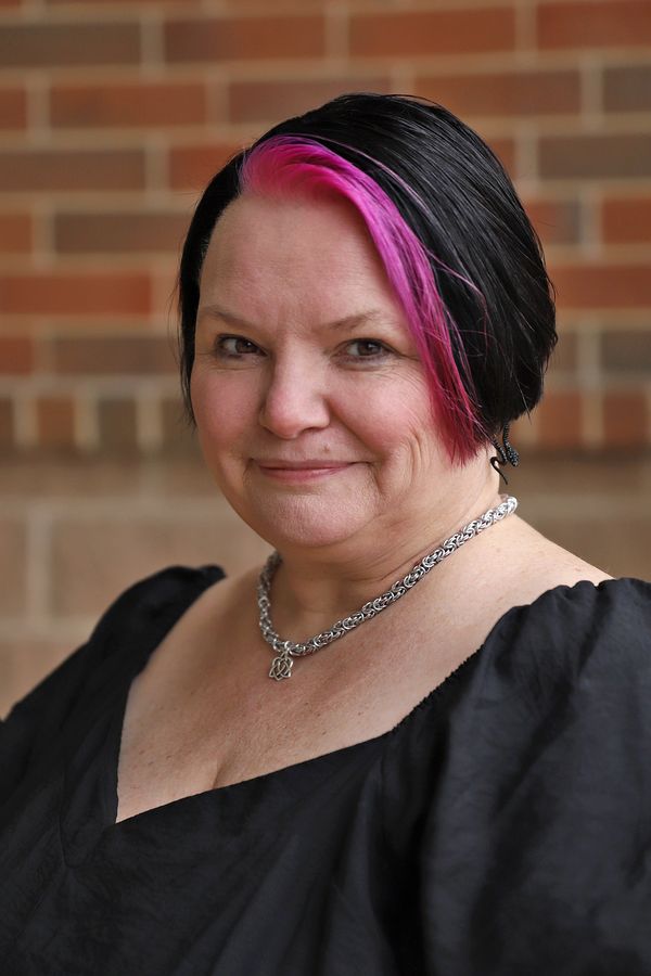 Woman with black and pink hair wearing a chain necklace and black dress.