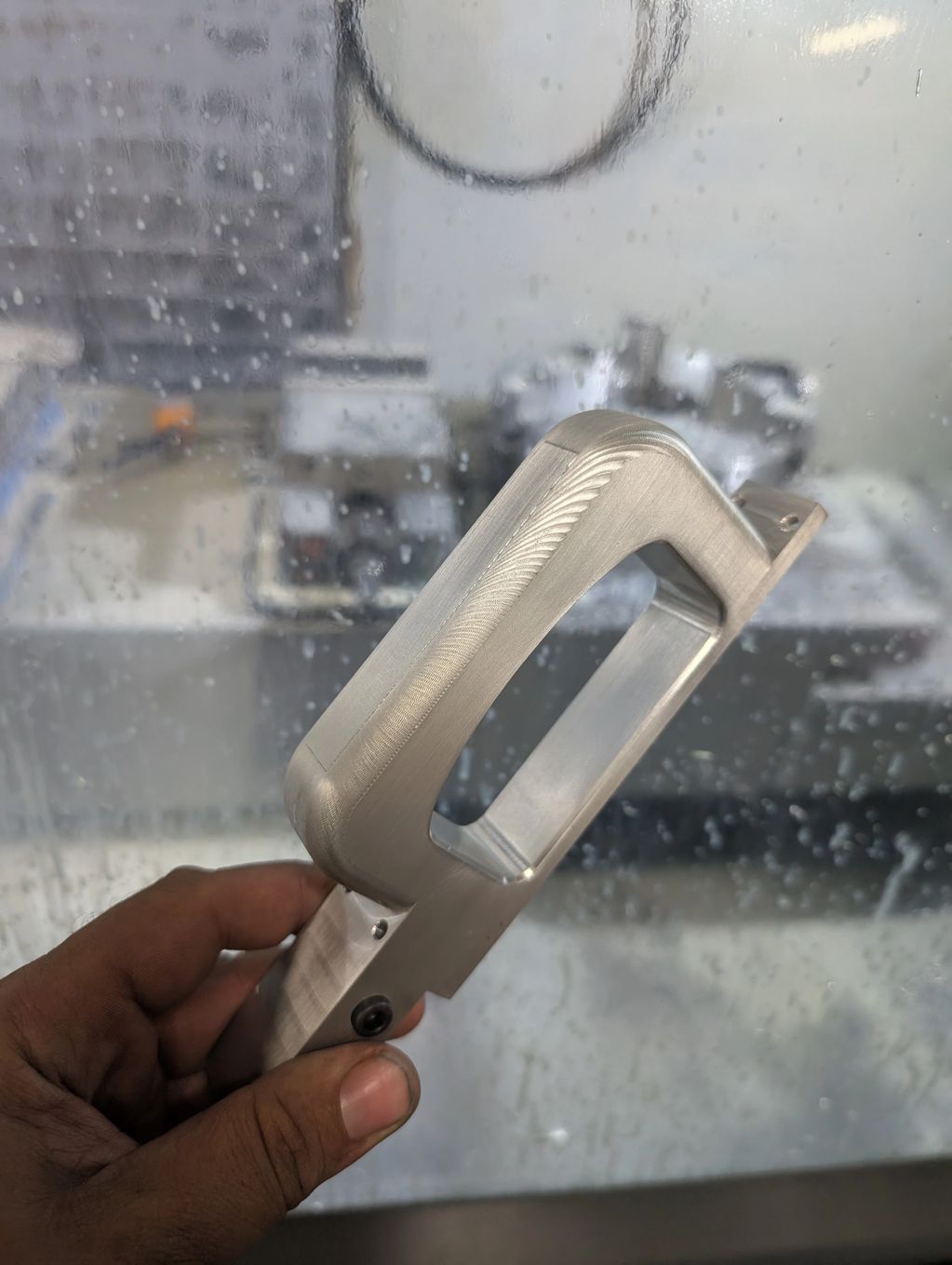 Hand holding a machined metal part with visible welding.