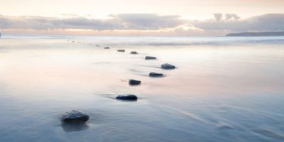 Stepping stones leading across calm water at sunset.