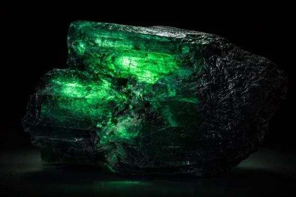 A raw emerald crystal glowing green against a black background.