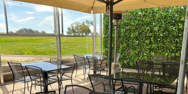 View of side patio space, with tables and chairs set up, plexiglass wall for weather, and an accent 