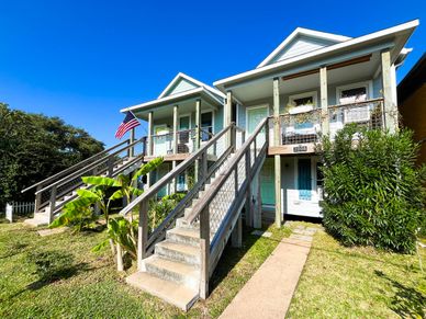 A bright blue house with two stairways and an American flag under a clear sky.