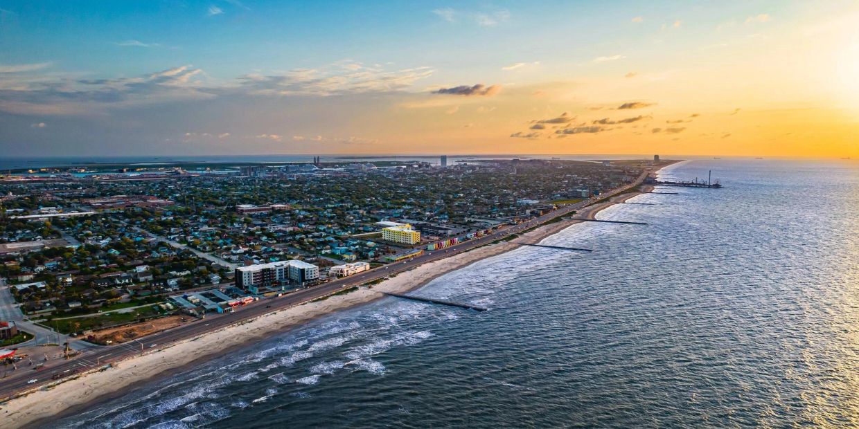 Aerial view of a coastal city at sunset with waves hitting the shore.