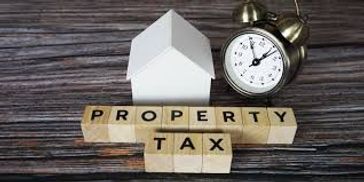 Wooden blocks spell out property tax next to a small house model and clock.
