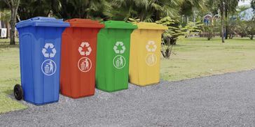 Four colorful recycling bins lined up outdoors on a pathway.