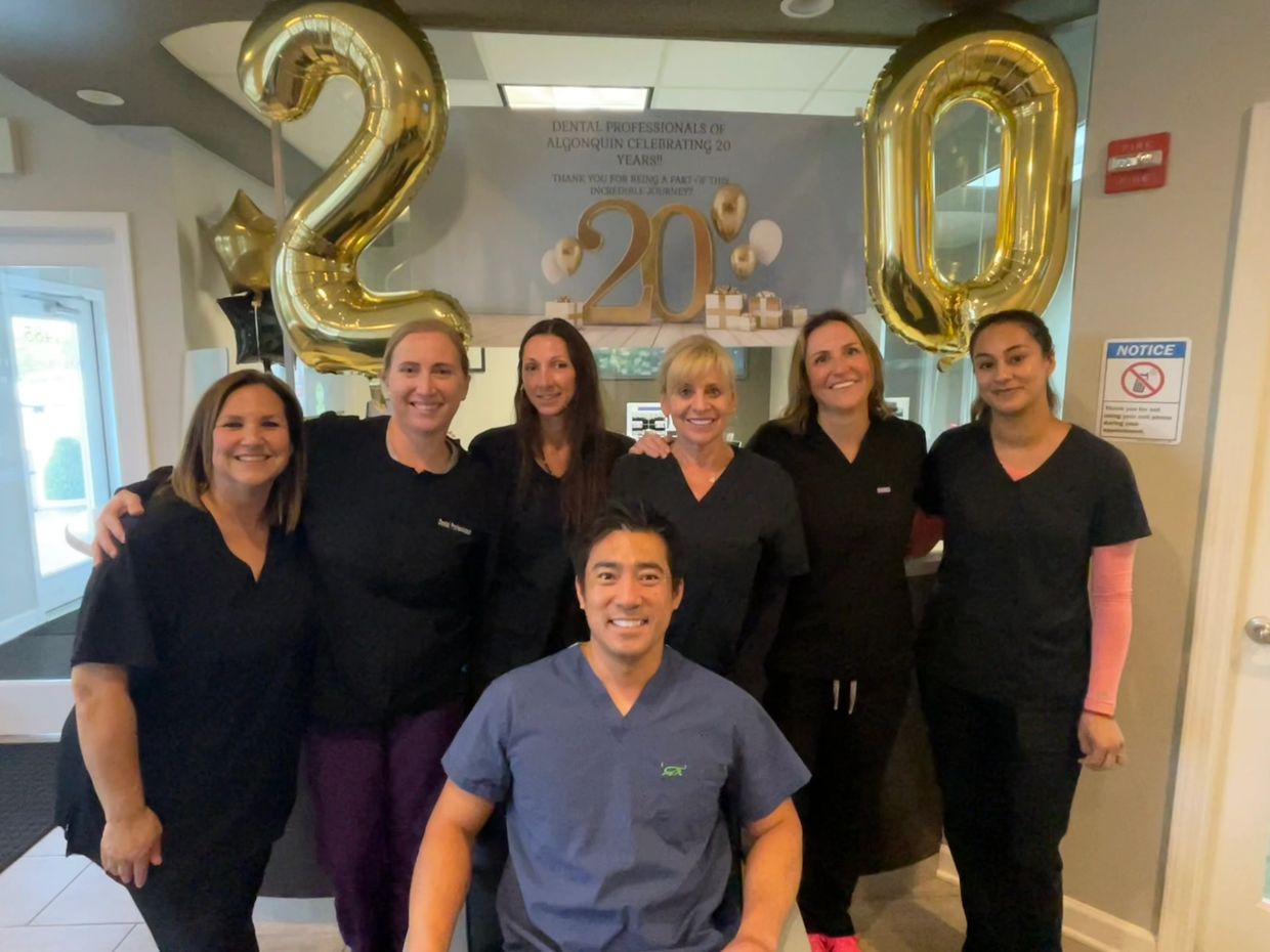 Dr. An sitting in front of his team with gold 20 year balloons and sign behind him.