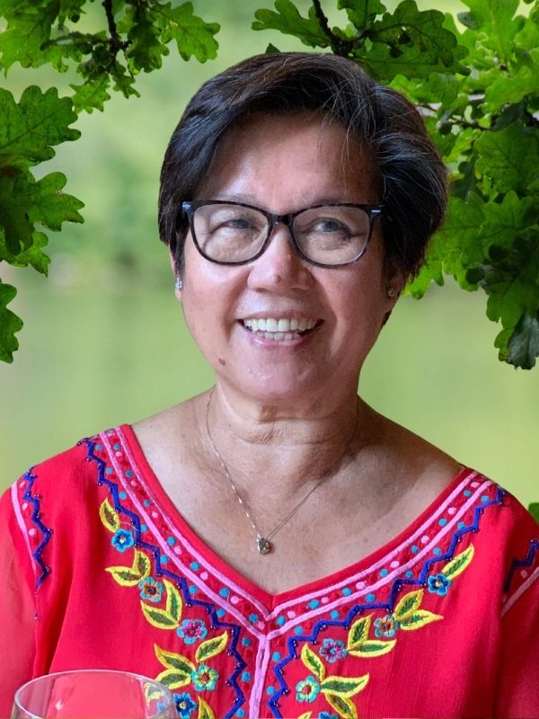 Helen Santos wearing glasses and smiling in a colorful, embroidered top.