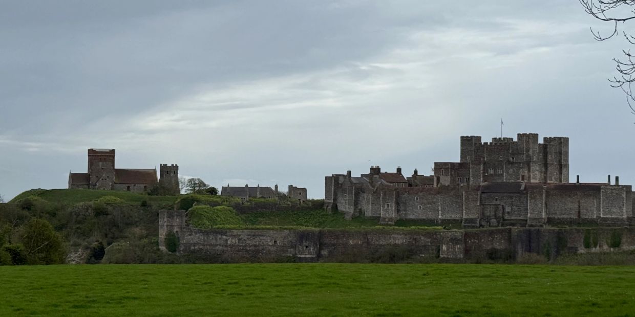 A large medieval castle with surrounding buildings under a cloudy sky.