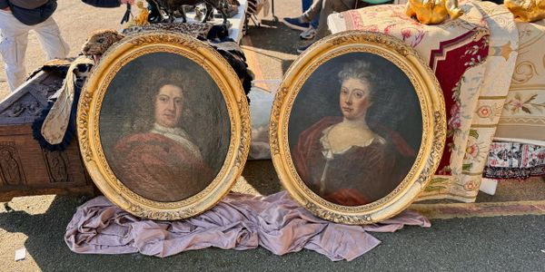 Two ornate oval portraits of a man and a woman displayed outdoors on a cloth.