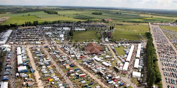 A large outdoor event with many tents, cars, and people in a rural area.
