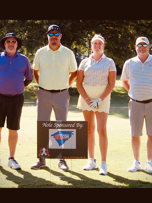 Four golfers standing behind a sponsorship sign on a sunny golf course.